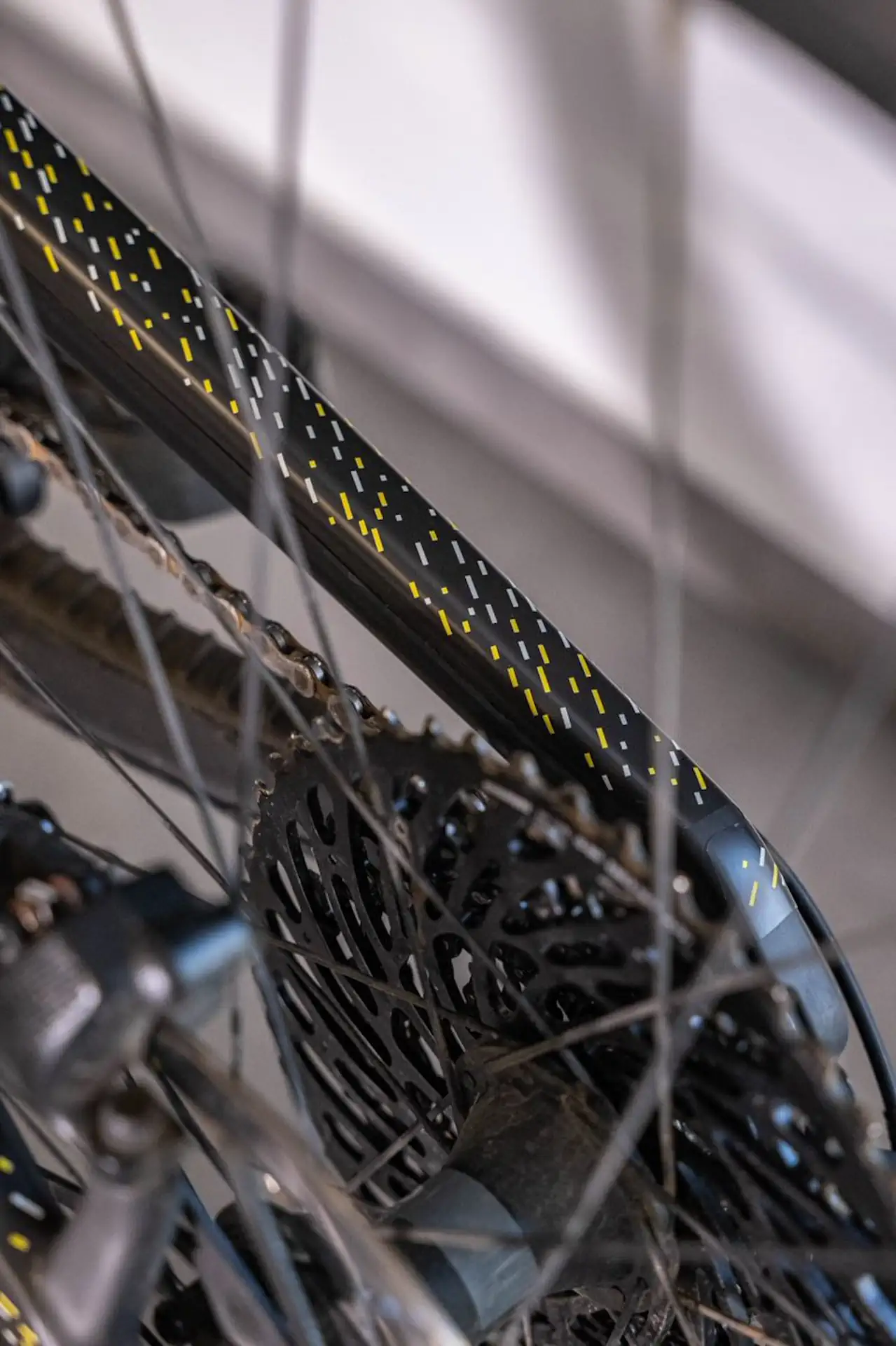 Szczegółowe zdjęcie koła rowerowego z czarną oponą i żółtymi detalami na tylnym trójkącie