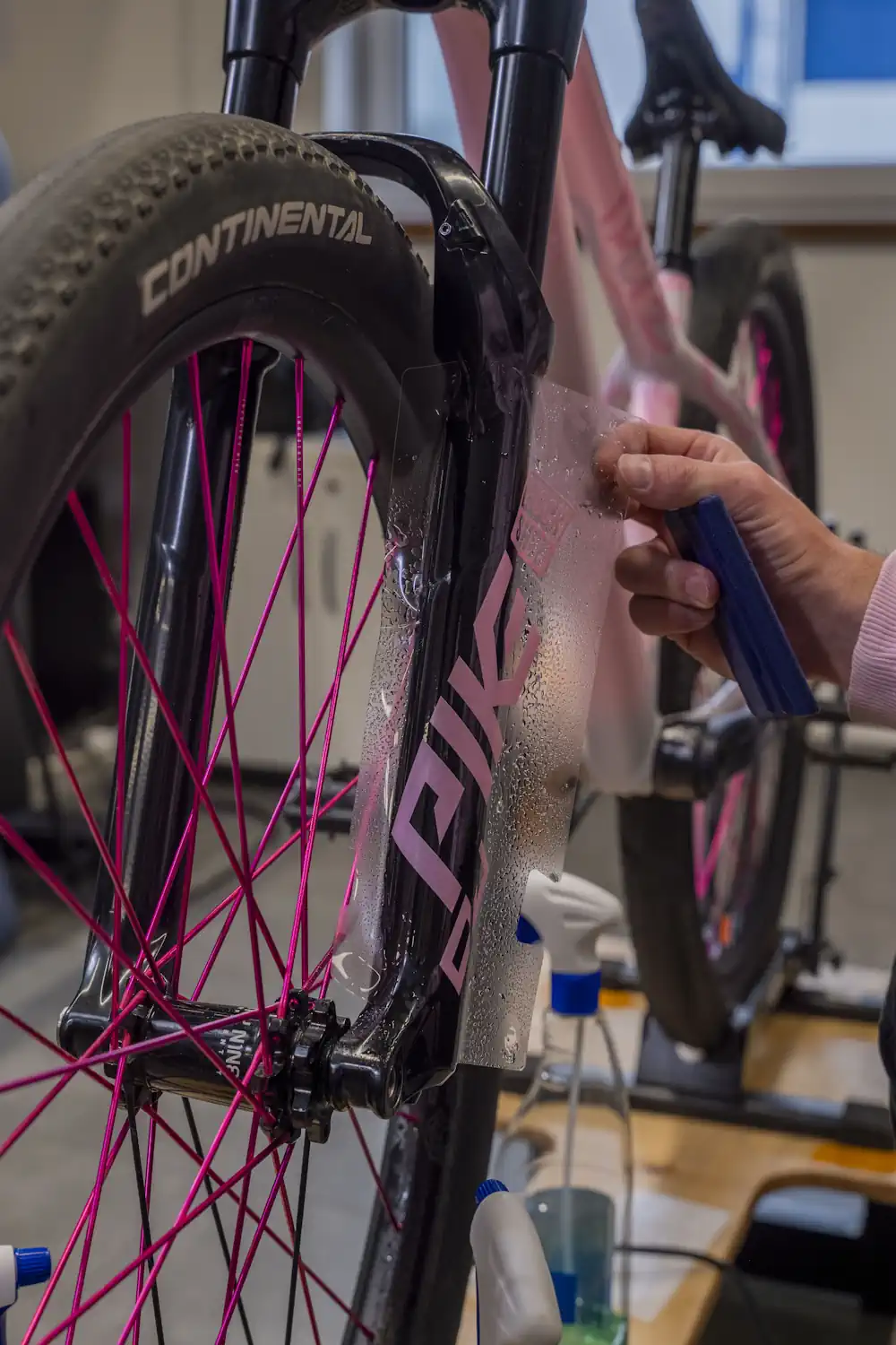 Ręce nakładają przezroczystą folię ochronną na przedni widelec różowego roweru